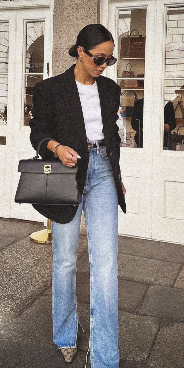 Femme en blazer noir, t-shirt blanc et jean bleu clair avec sac noir.