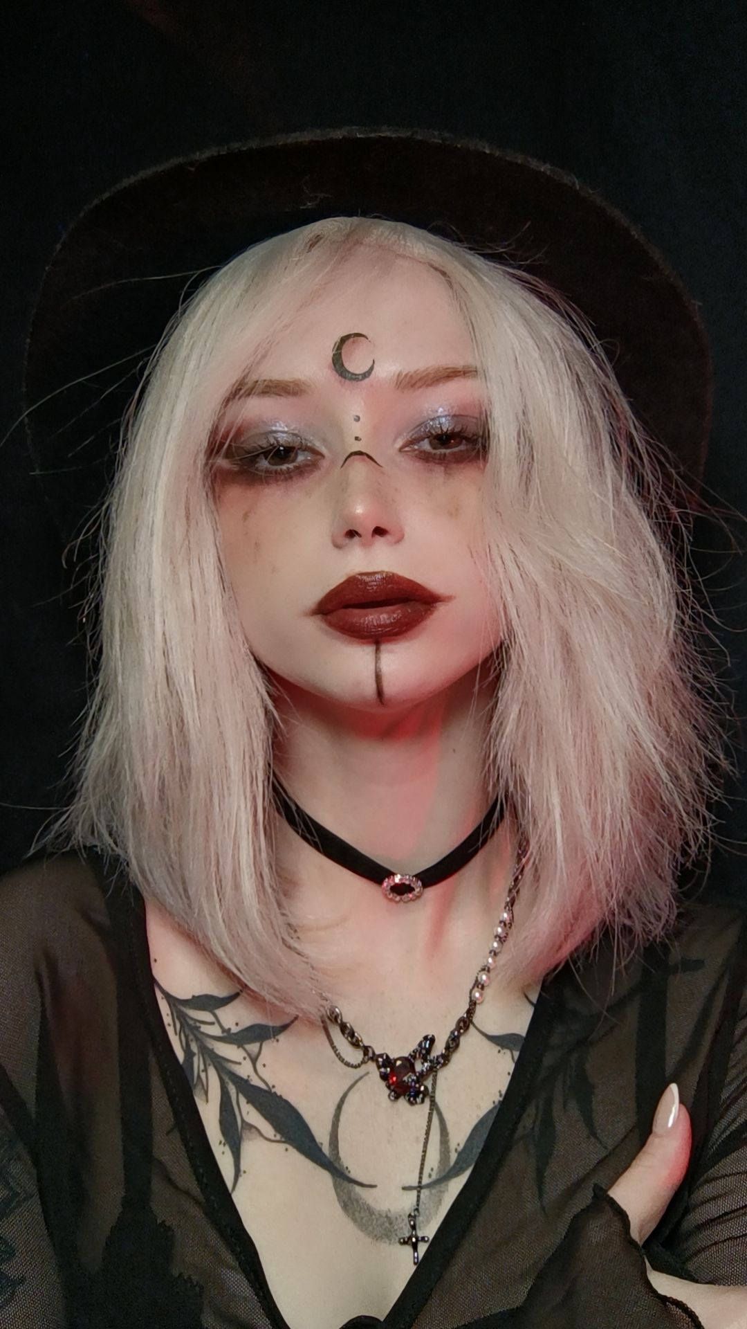 Visage maquillé avec lune noire et lèvres bordeaux, chapeau noir.